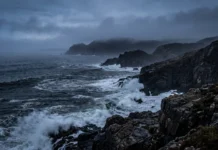 A moody, fog-shrouded rocky coastline at twilight.